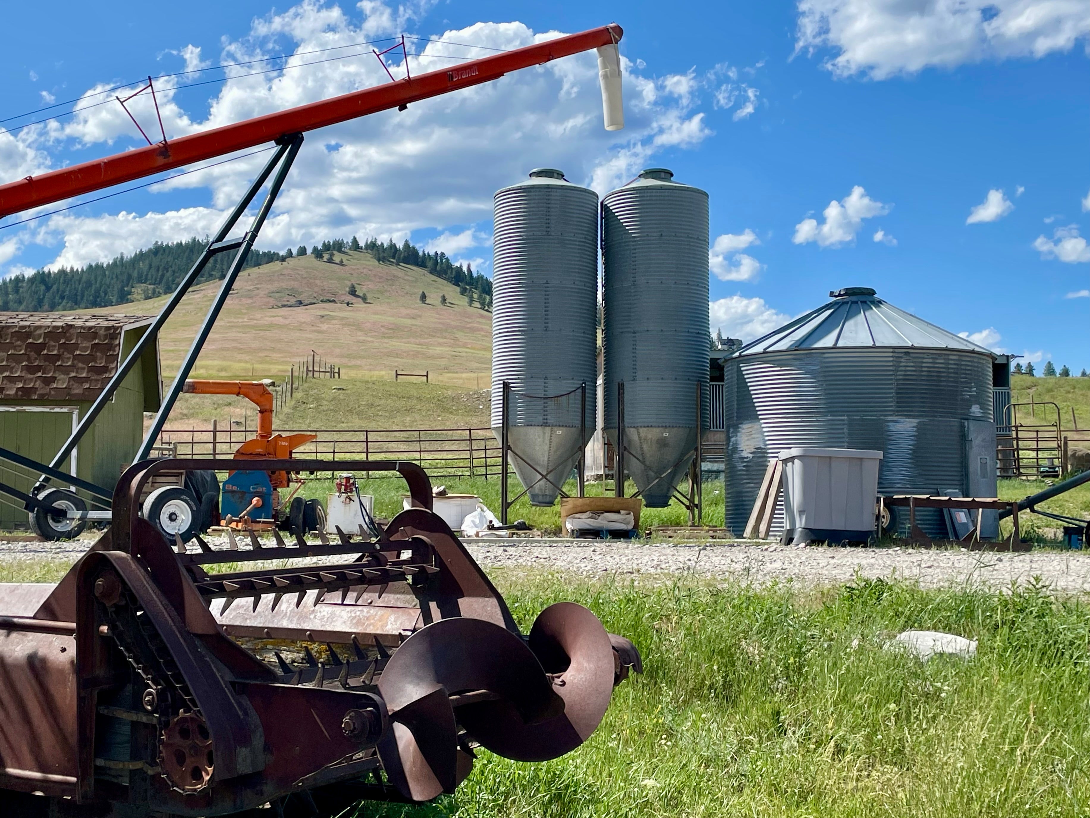 Farm equipment and silos on a rural landscape with a blue sky.